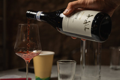 Mano sirviendo un Langhe Nebbiolo de Agricola Brandini en una copa, sobre una mesa de mármol con luz cálida de bar